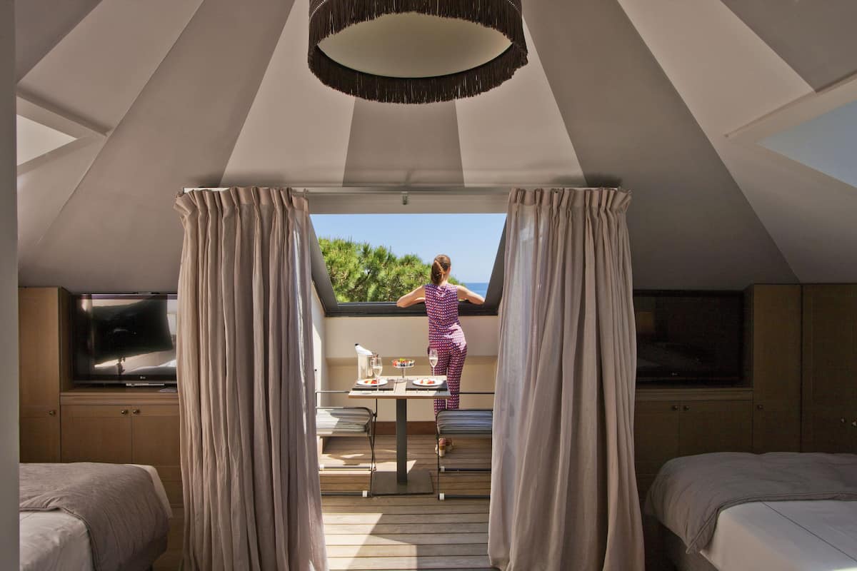 A bedroom with a large window, a bed, a TV, and a table with a chair.