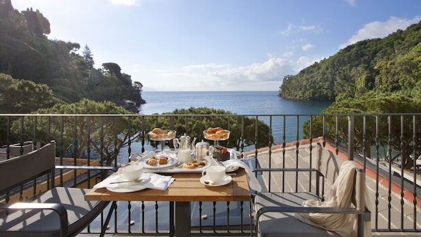 Una mesa preparada para el desayuno con una vista panorámica del mar y las colinas.