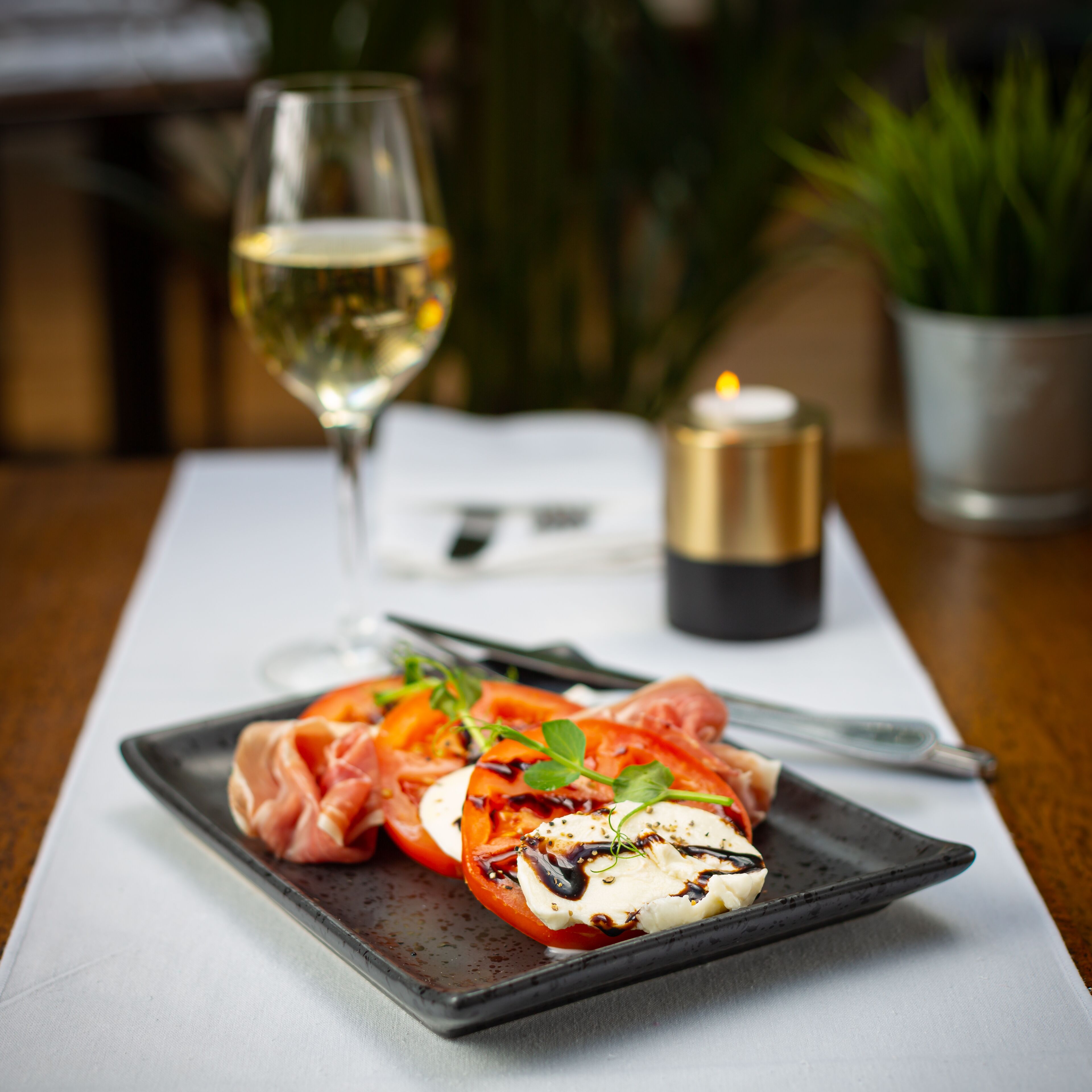 A plate of food with a glass of white wine and a candle on a table.