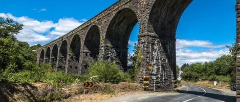 A stone viaduct with multiple arches over a road, surrounded by greenery.