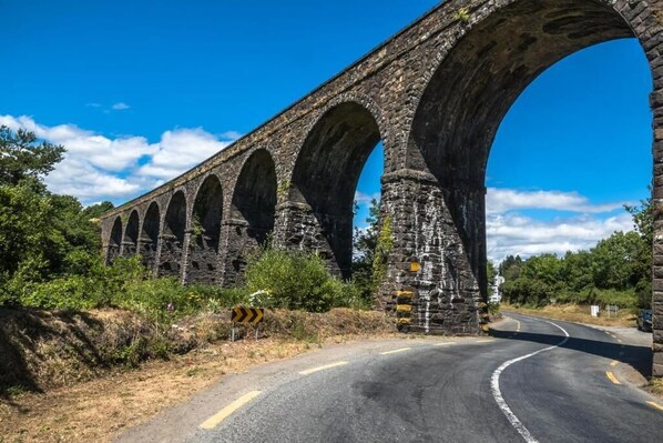 Un viaducto de piedra con múltiples arcos sobre una carretera, rodeado de vegetación.