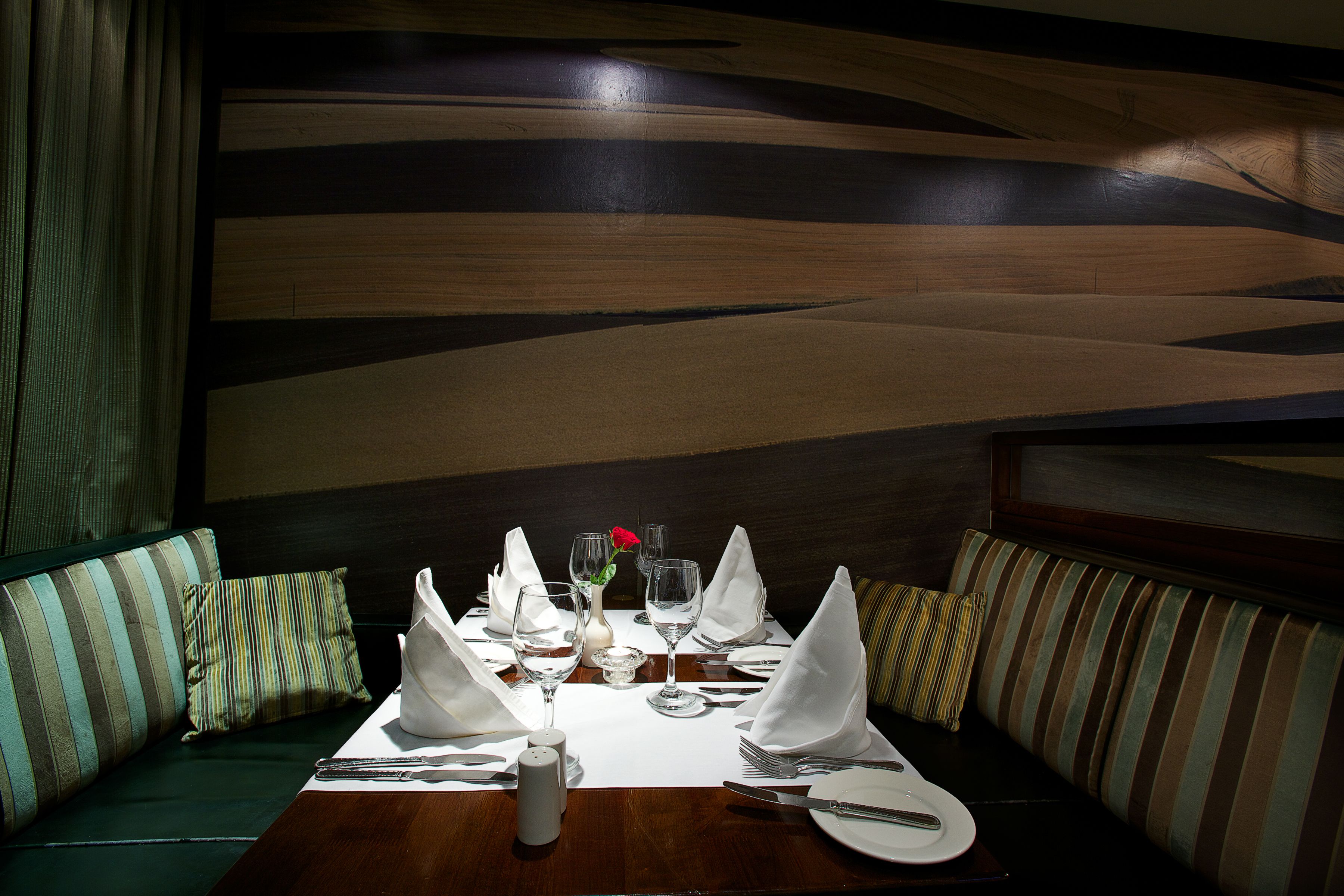 A dining table set with white napkins, silverware, and wine glasses, with a vase of flowers and a salt and pepper shaker.