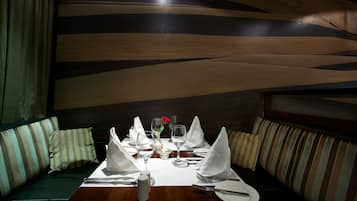 Een eettafel gedekt met witte servetten, bestek en wijnglazen, met een bloevas en zout- en peperstel.