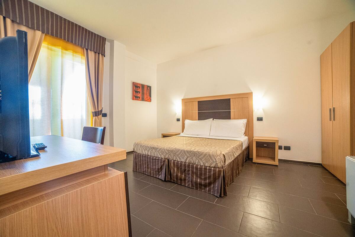Una habitación de hotel con cama, mesitas de noche, un escritorio con silla y un armario.
