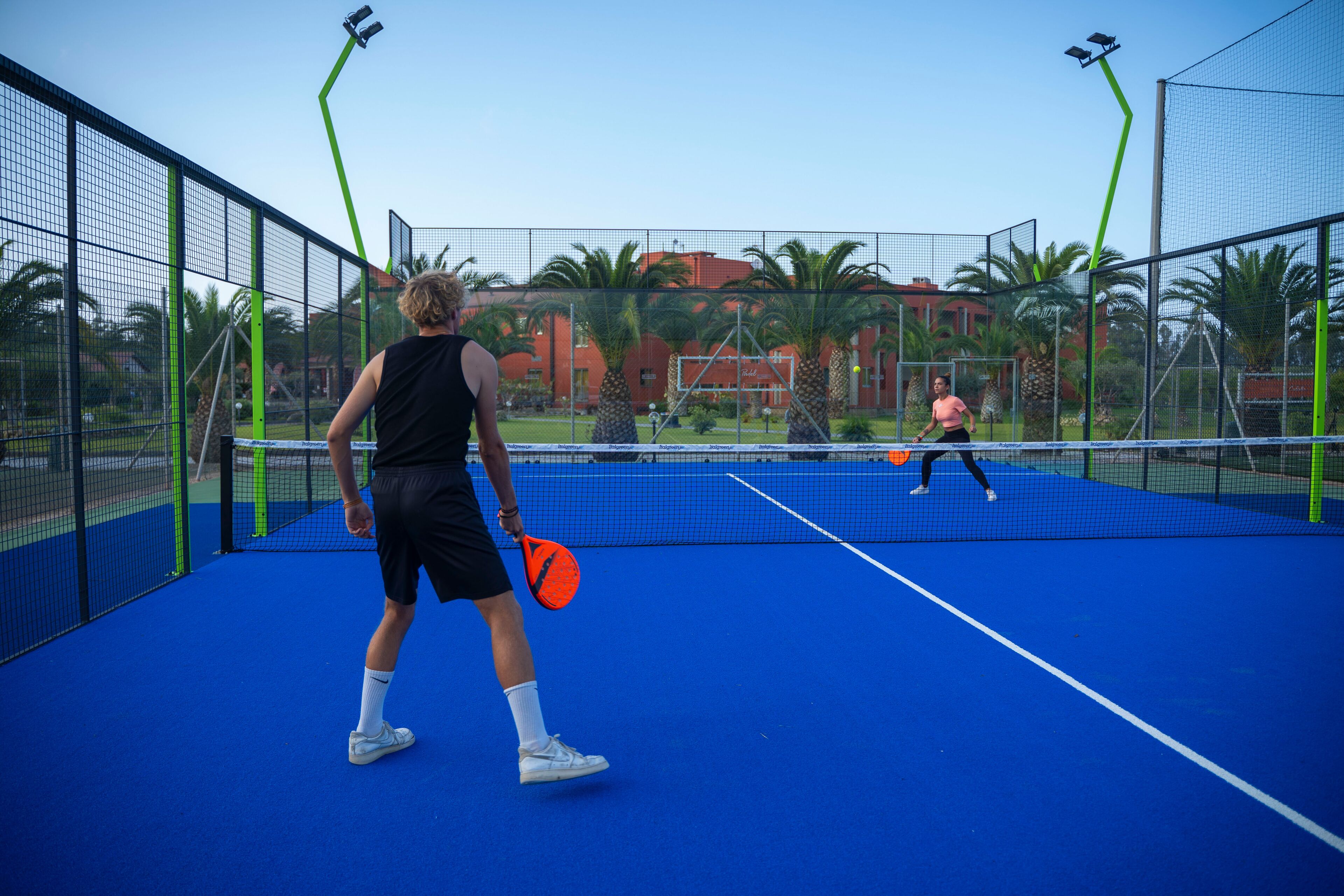 Un court de tennis avec un filet, deux joueurs et un bâtiment en arrière-plan.