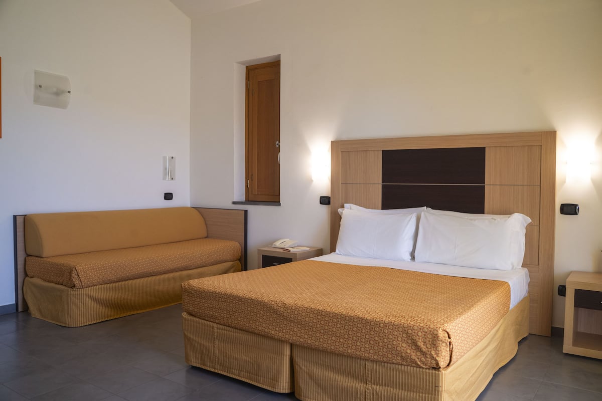 Una habitación de hotel con una cama, un sofá, una mesita de noche y un buró.
