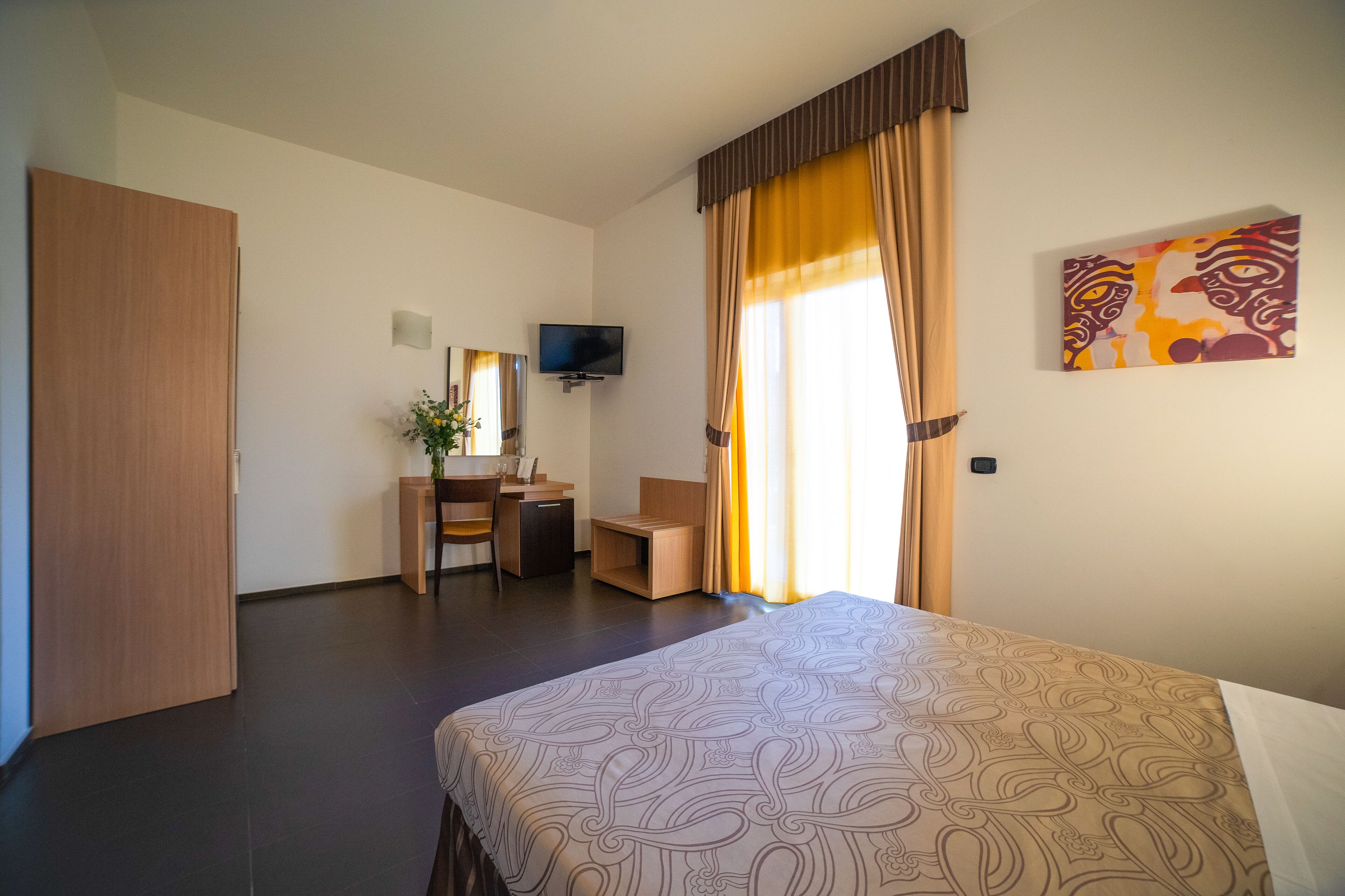 A hotel room with a bed, a desk, a chair, a television, and a painting on the wall.