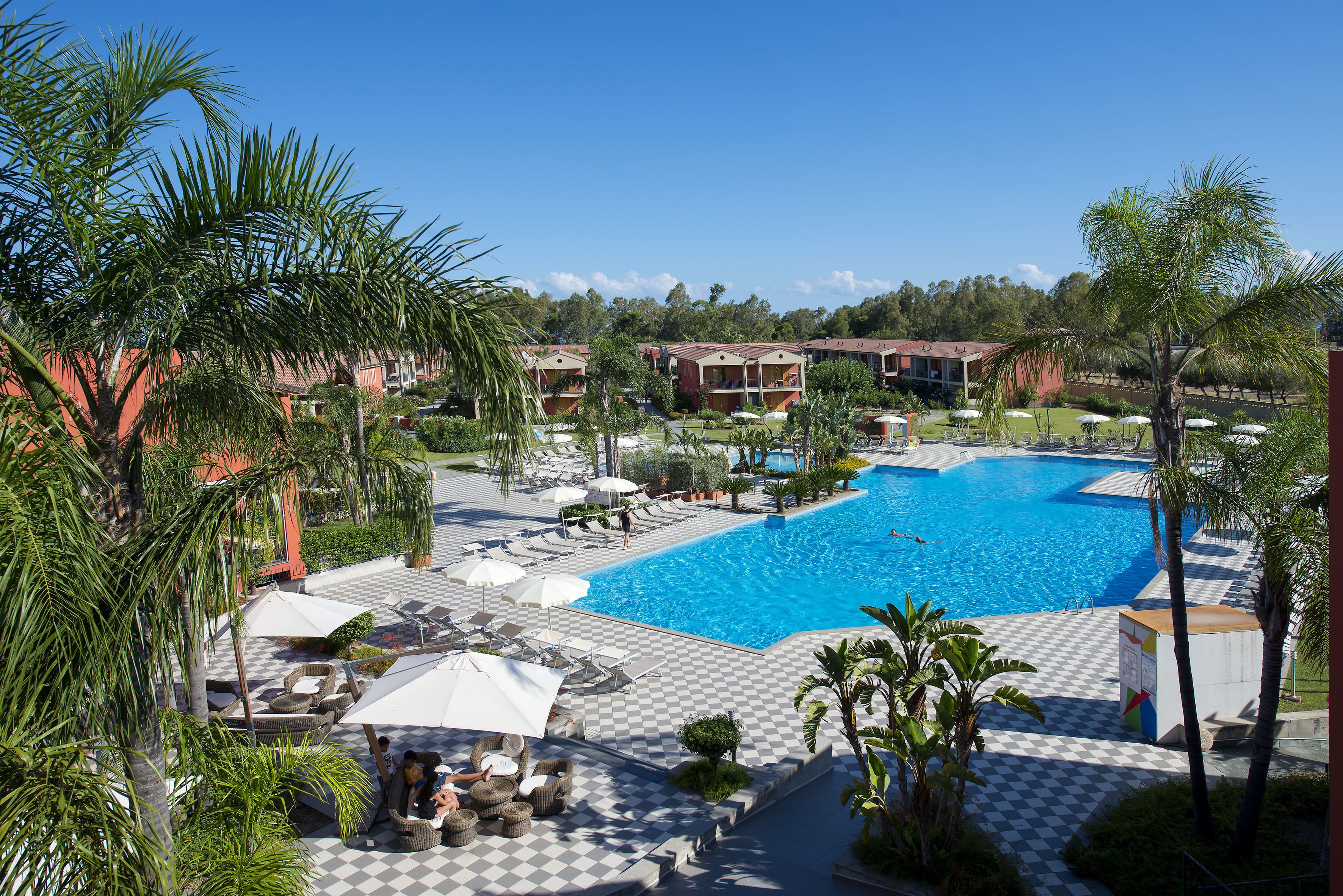 A resort with a large swimming pool, lounge chairs, and palm trees.