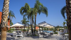 Un área de piscina al aire libre con suelo a cuadros, sillas reclinables blancas y sombrillas.