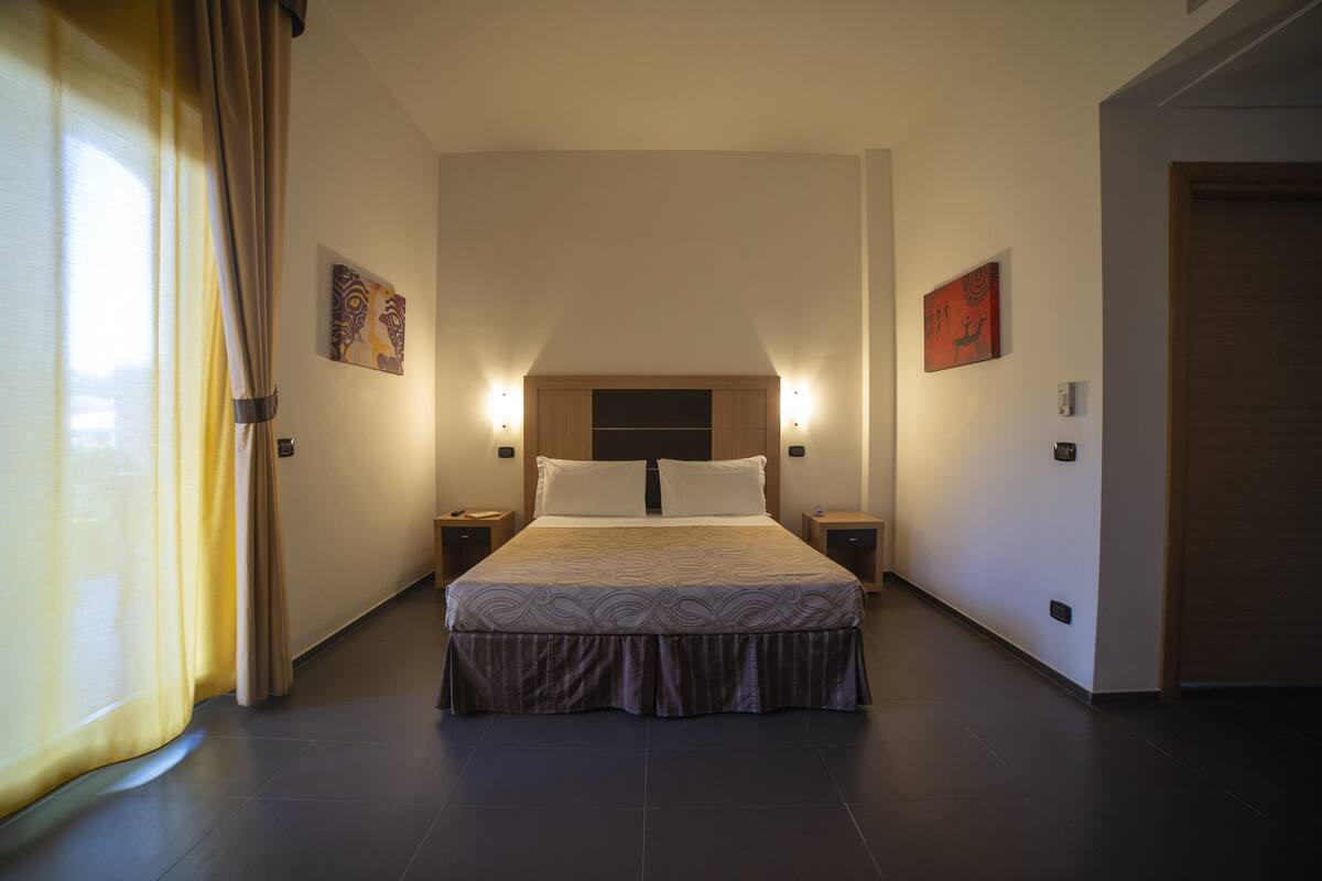 Habitación de hotel con una cama grande, dos mesitas de noche, un cabecero y dos luces fijadas a la pared.