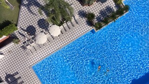 Vista aérea de una piscina con suelo de ajedrez, sillas de descanso y palmeras.