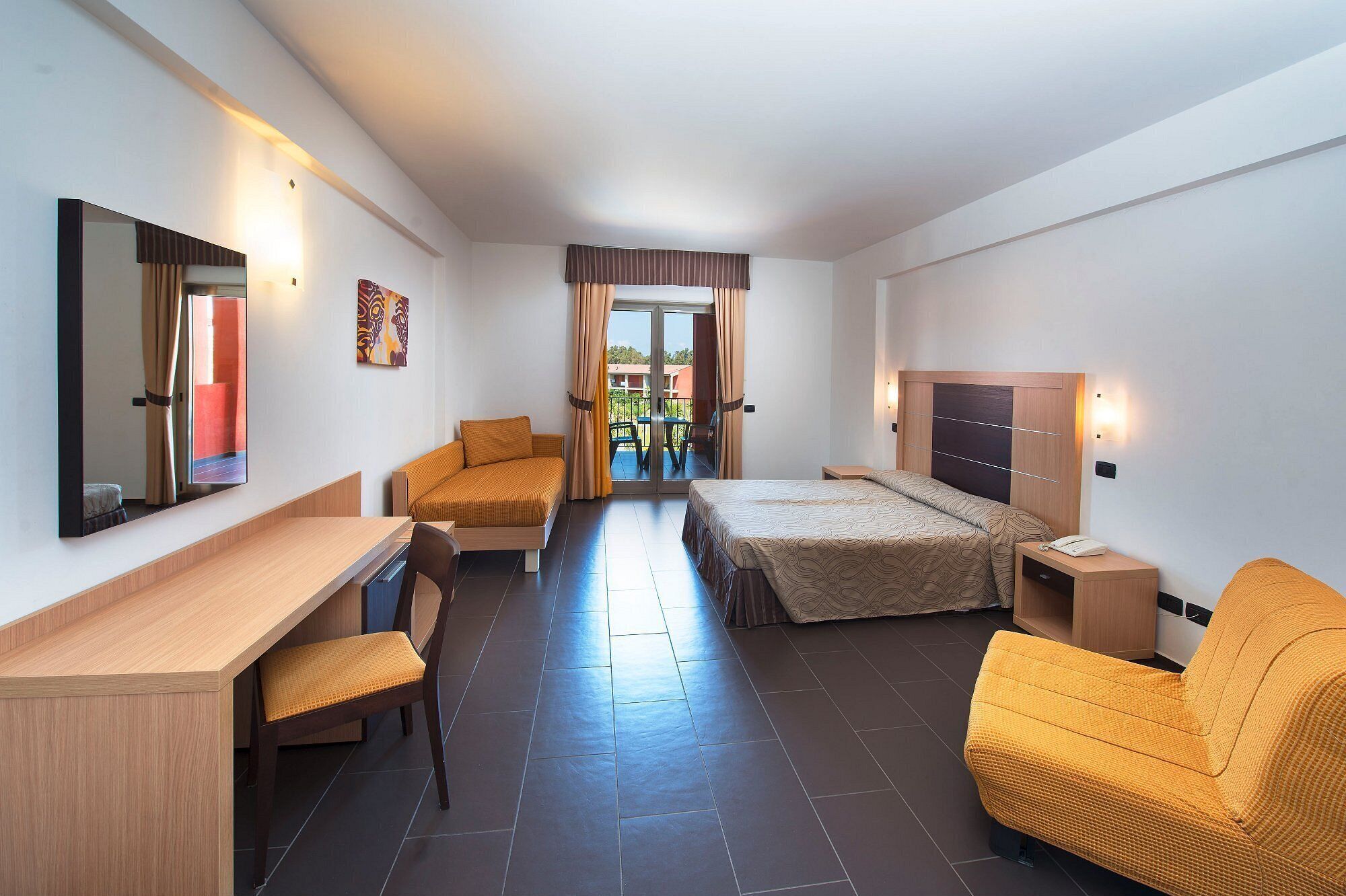 Habitación de hotel con cama, escritorio, silla, mesita de noche, espejo y vistas al exterior.