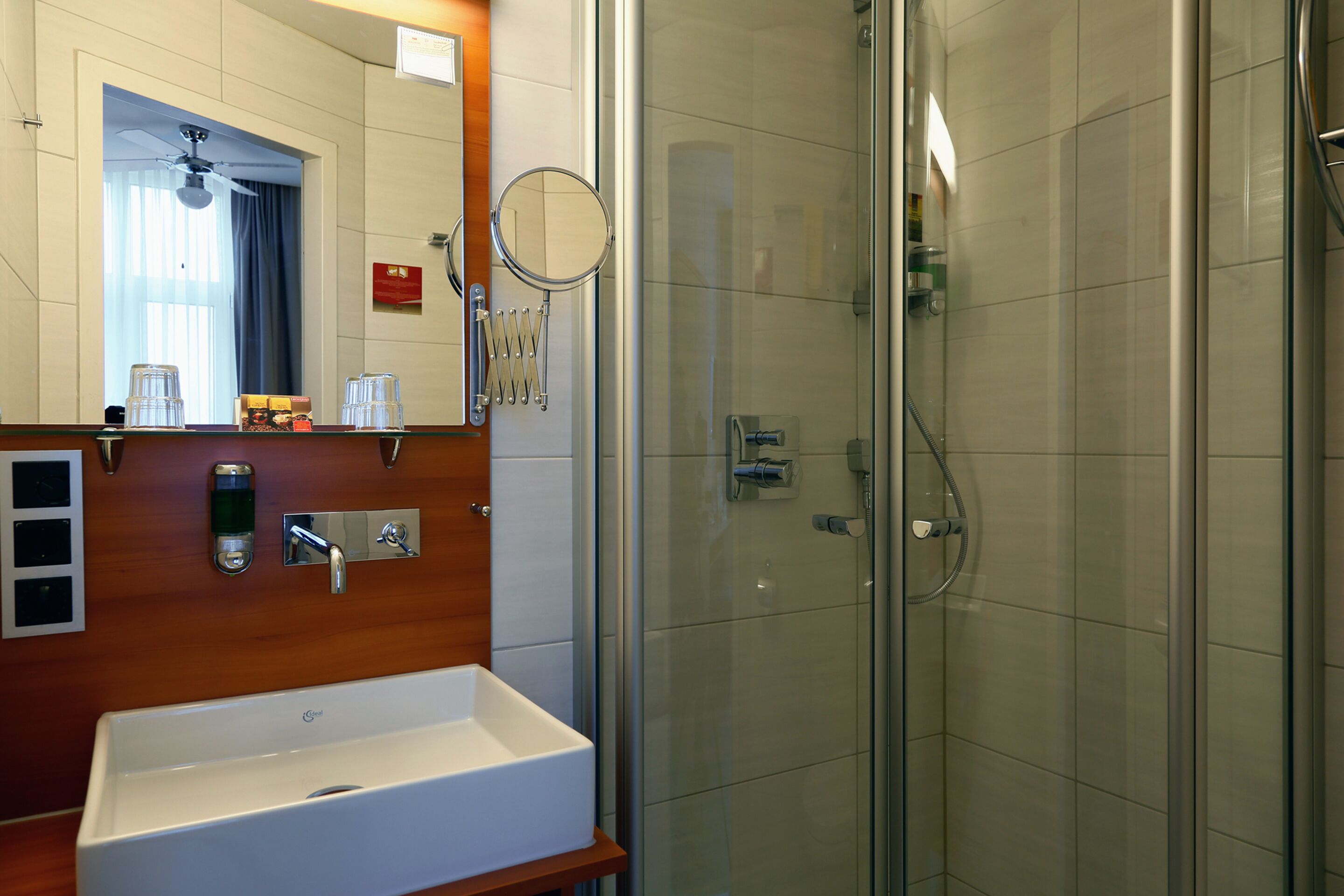 A modern bathroom with a white sink, a mirror, and a glass-enclosed shower.