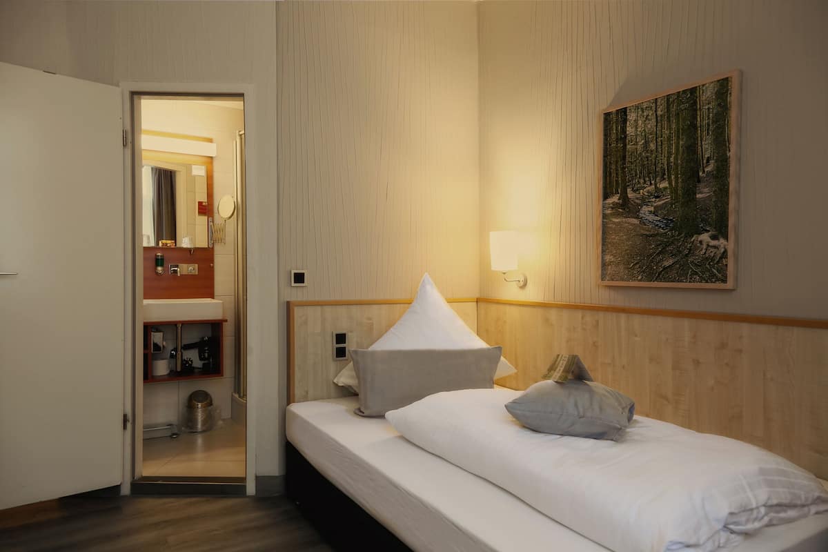 Une chambre d’hôtel comprenant un lit, une table de chevet, un miroir, un tableau et une porte donnant sur une salle de bain.
