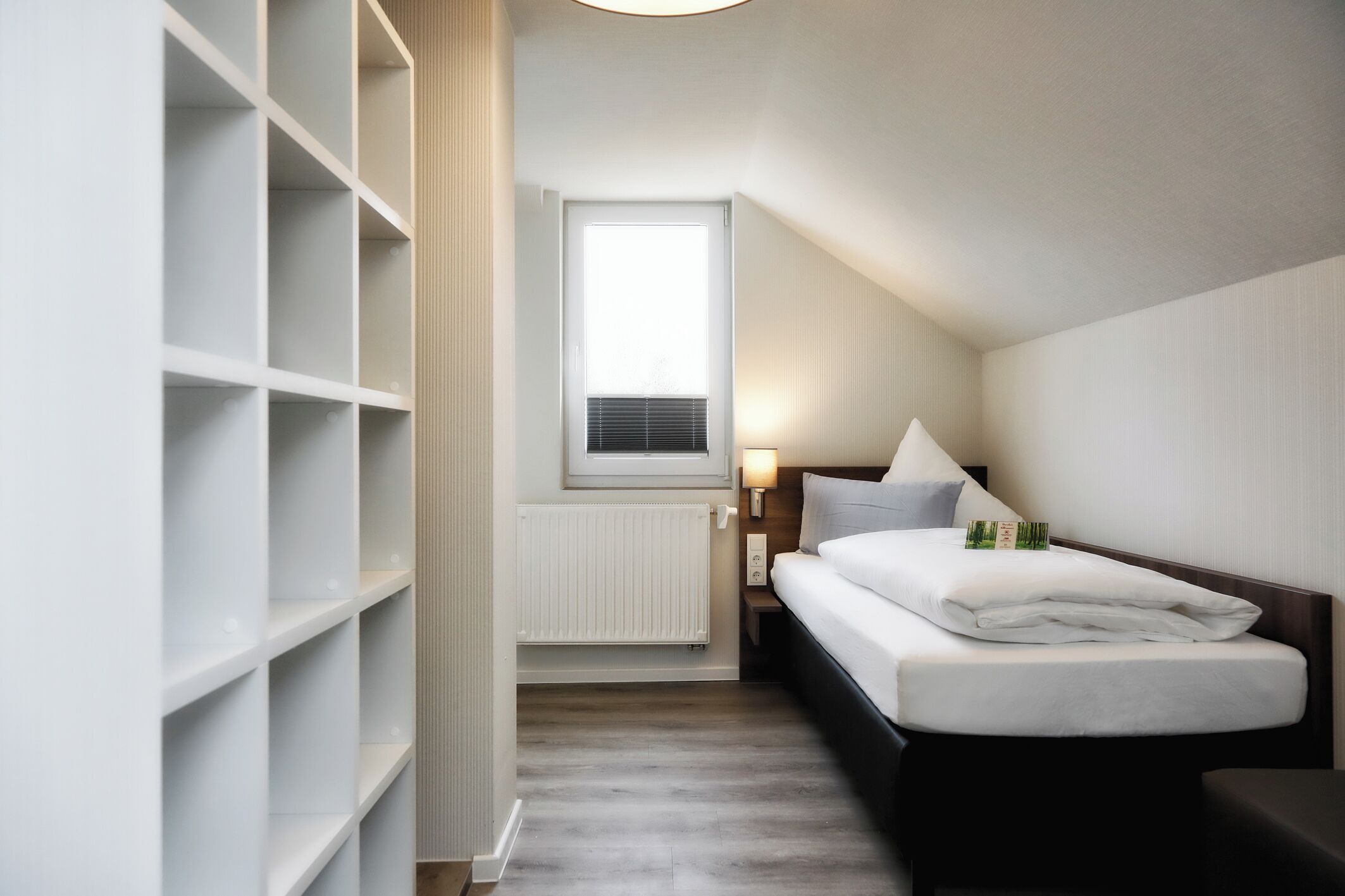 A bedroom with a bed, a nightstand, a window, and built-in shelving.