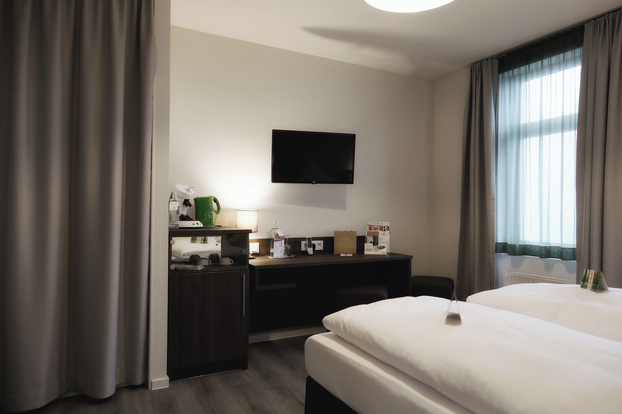 Ein Hotelzimmer mit Bett, Schreibtisch, Flachbildfernseher, Lampe und einem Fenster mit Vorhängen.