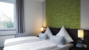 A hotel room with two beds, a window with curtains, a green textured wall, and two bedside lamps.