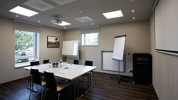 A conference room with a white table, black chairs, a projector, a whiteboard, and a black speaker.