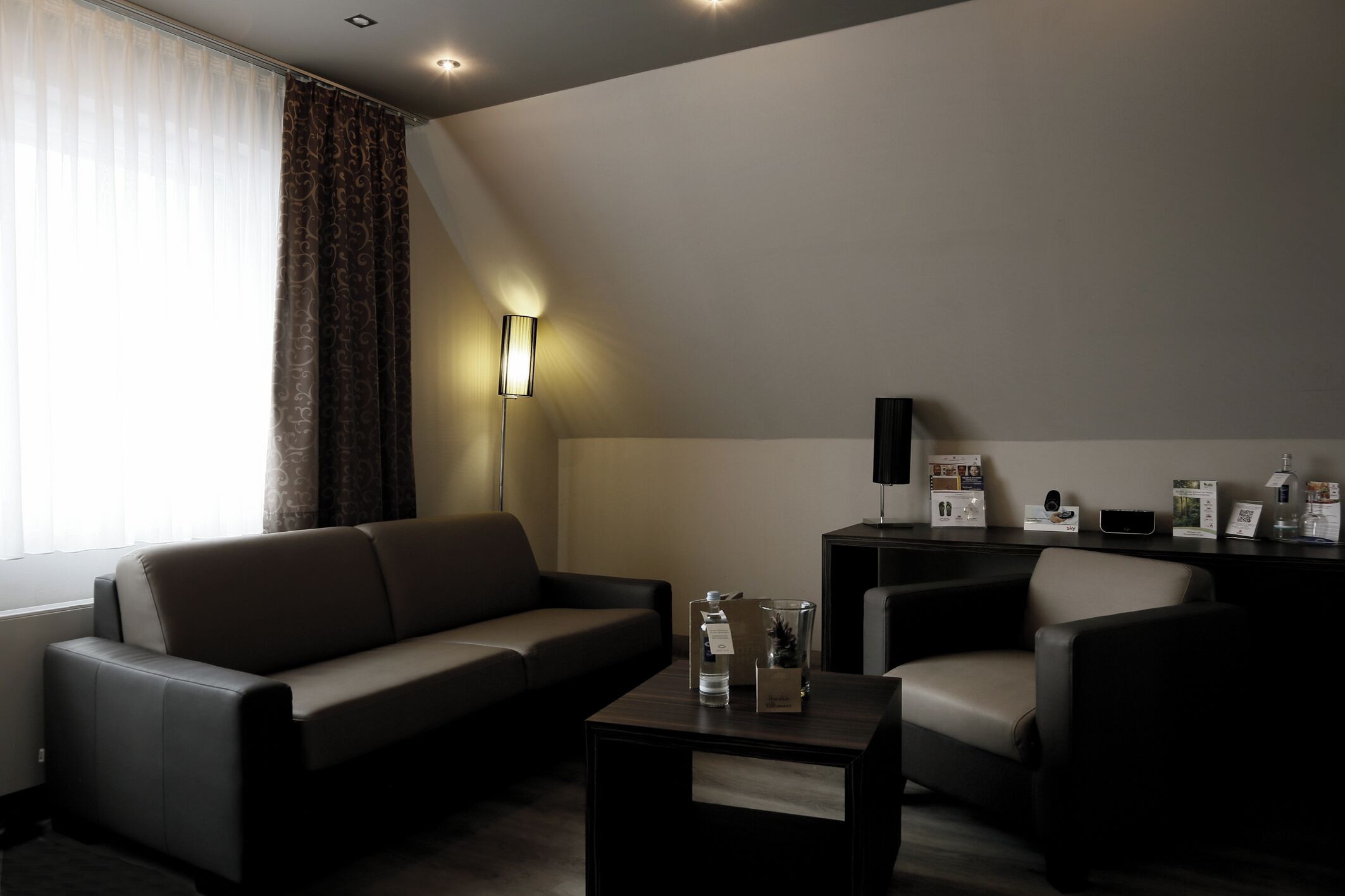 Ein modernes Hotelzimmer mit einer Couch, einem Sessel und einem kleinen Tisch mit Annehmlichkeiten.