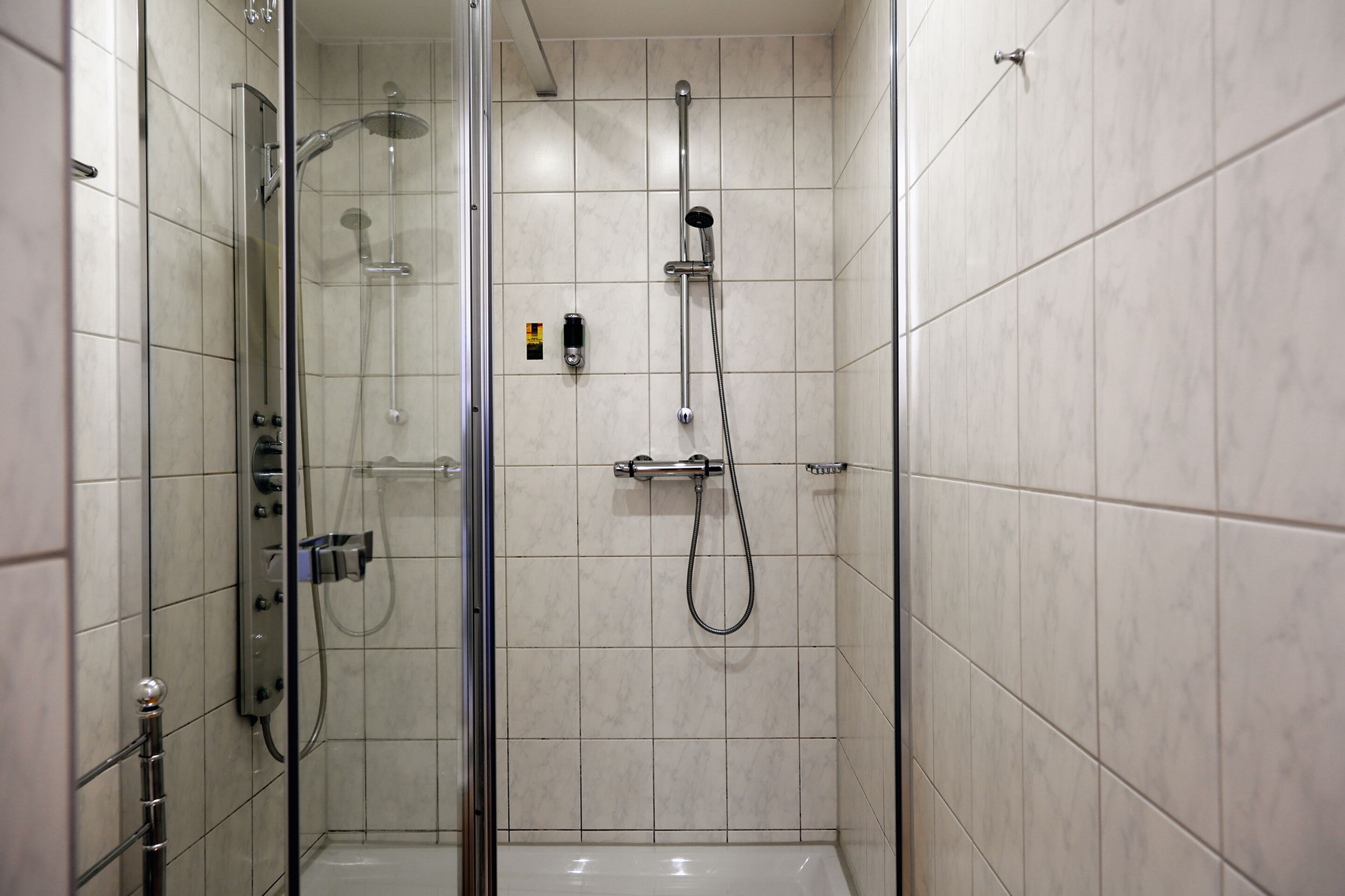 Ducha moderna con mampara de vidrio, ducha de mano y grifo empotrado.