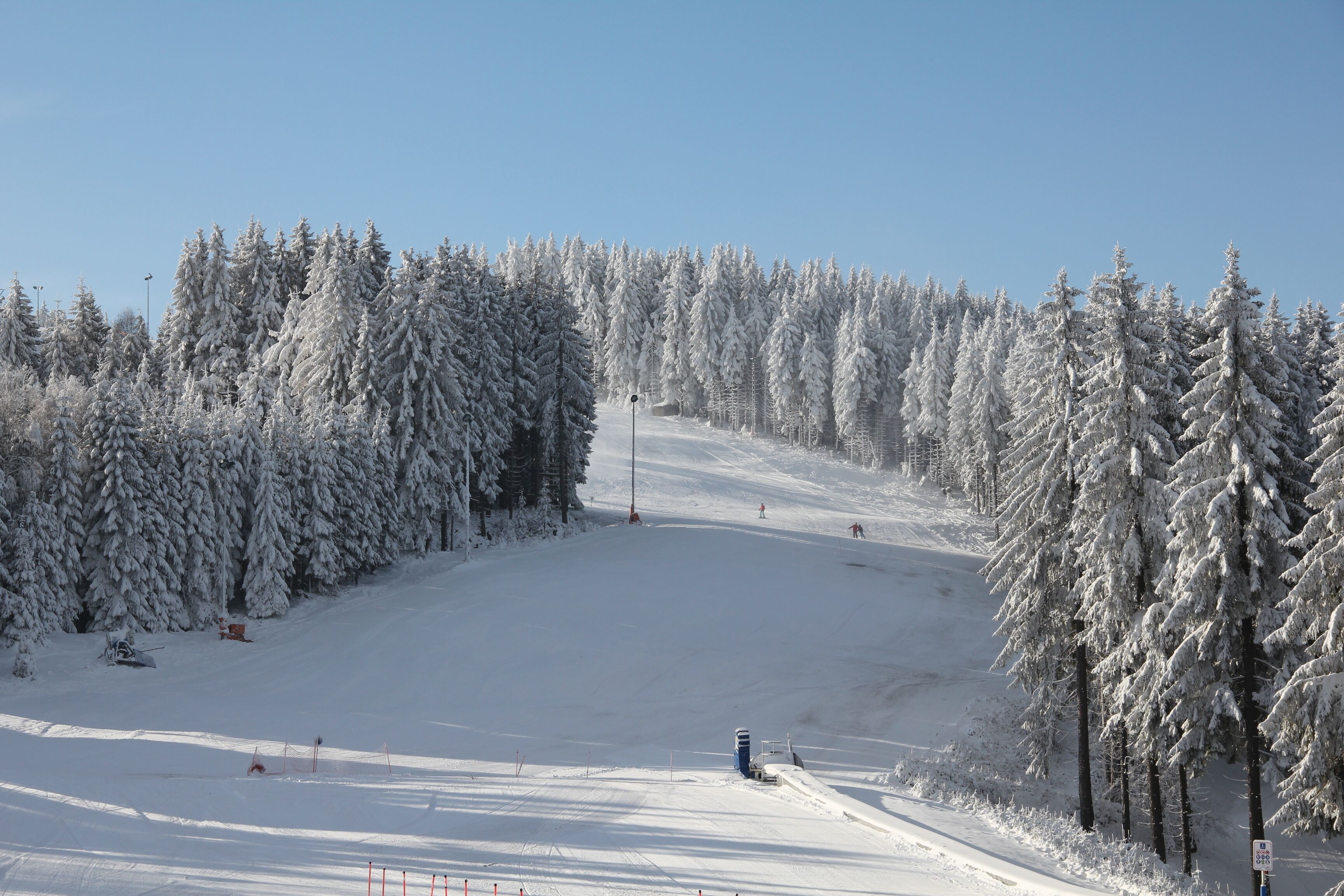 A snow-covered ski slope with trees on both sides and a clear sky.