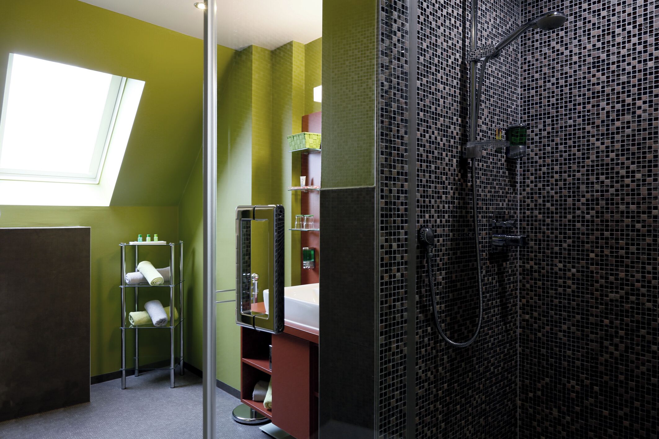 A bathroom with a skylight, a shower with a mosaic wall, and a towel rack.