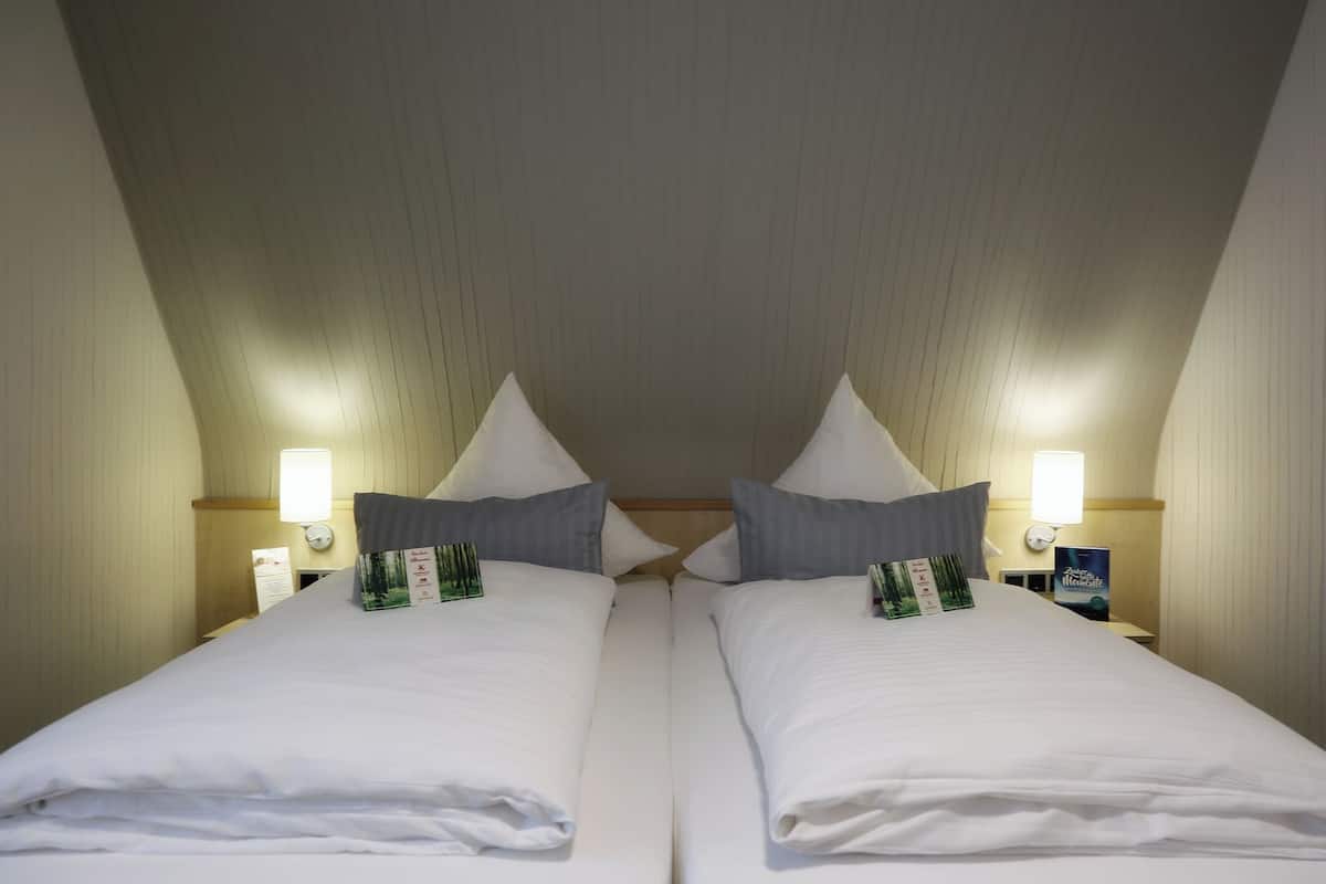 Une chambre d’hôtel avec deux lits, chacun agrémenté de draps et d’oreillers blancs, ainsi que de tables de chevet avec des lampes et des magazines.