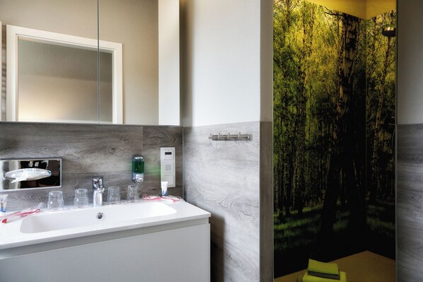 A modern bathroom with a white sink, mirror, and a wall-mounted shower.