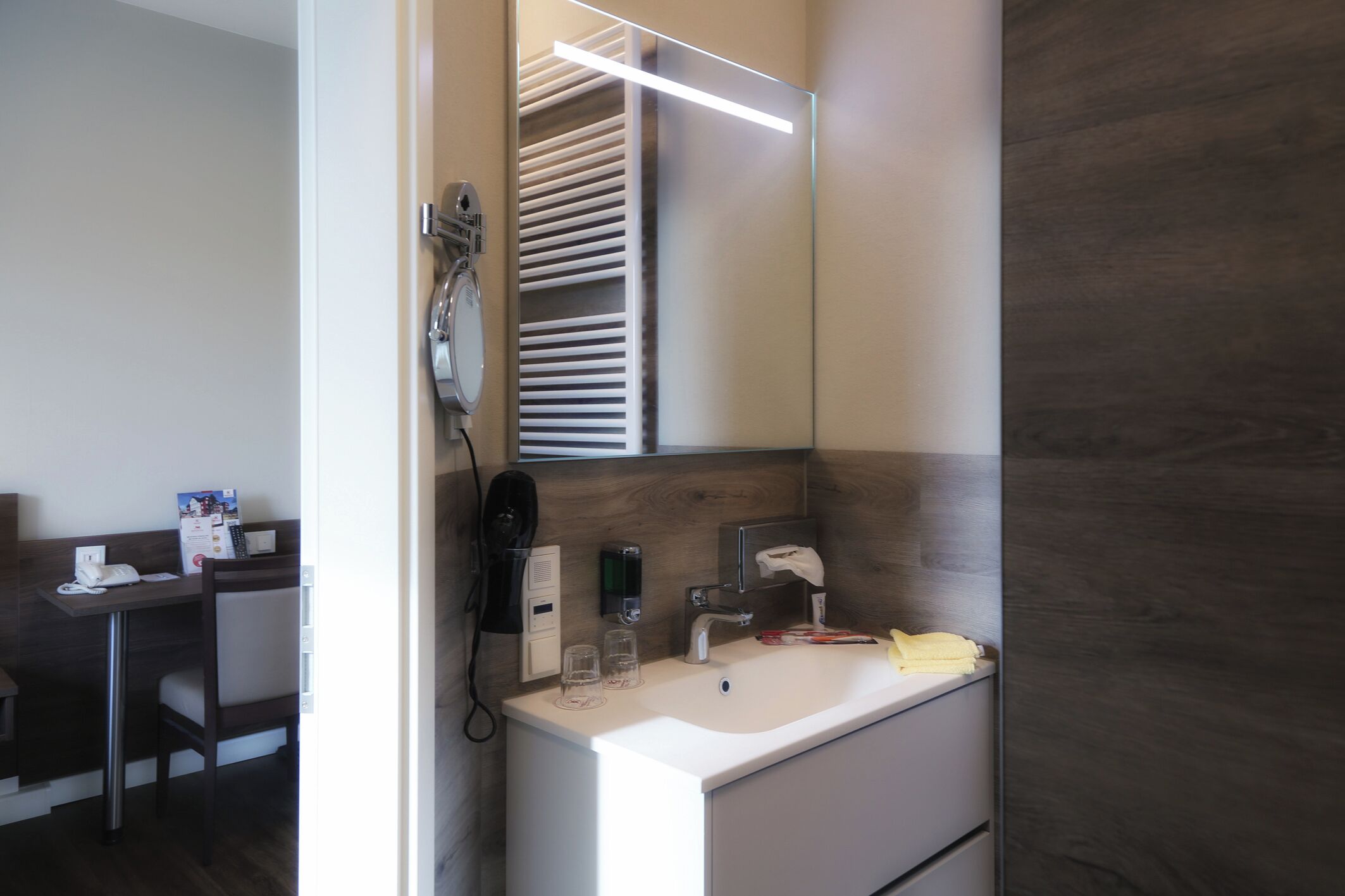A modern bathroom with a white sink, a mirror, a towel rack, and a hairdryer.