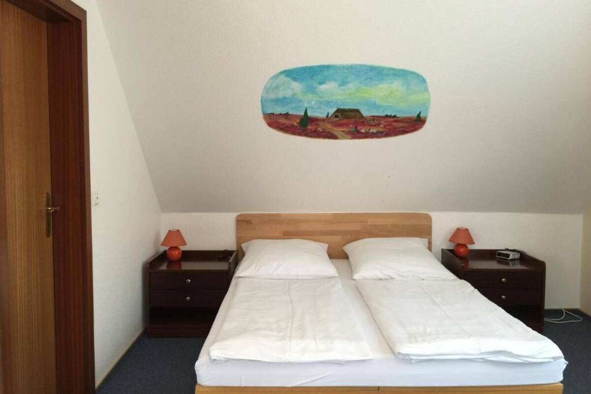 A room with a wooden bed, two bedside tables with lamps, and a wall painting.