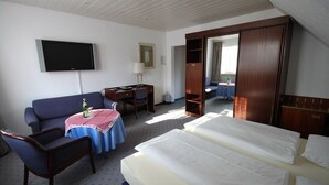Una habitación de hotel con cama, escritorio, sillón, televisor y espejo.