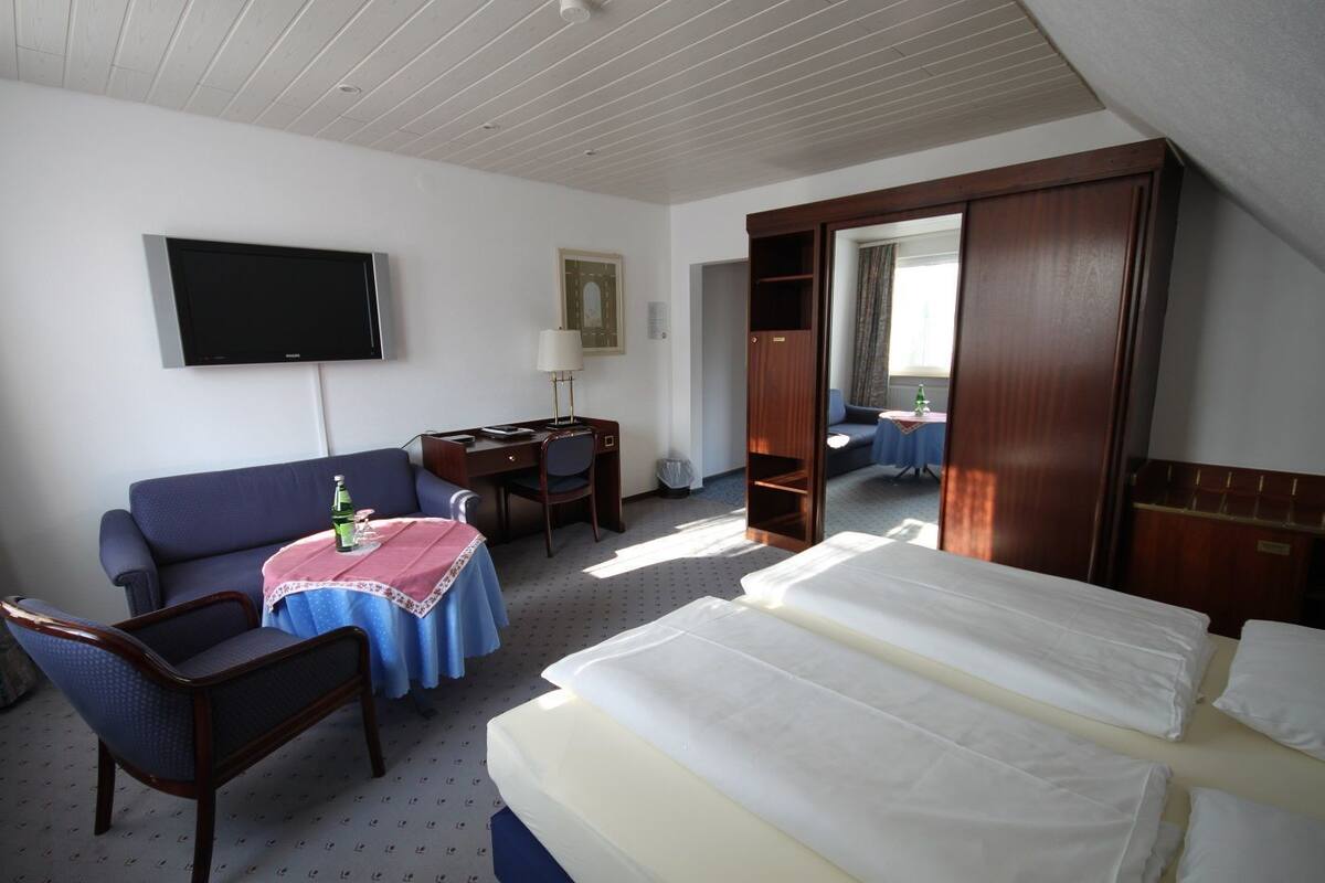 A hotel room with a bed, a desk, a chair, a sofa, a TV, and a mirror.
