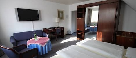 Una habitación de hotel con cama, escritorio, sillón, televisor y espejo.