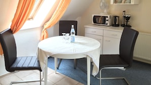 Una pequeña kitchenette con microondas, cafetera y armarios. Hay una mesa con sillas y una botella de agua.