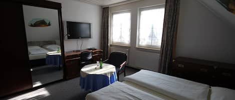 Et hotelværelse med seng, skrivebord, stol, fjernsyn og et vindue med gardiner.