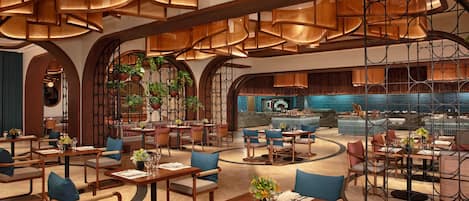 Interior moderno de restaurante con techos altos, mobiliario de madera y plantas colgantes.