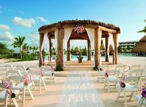A wedding ceremony setup with a wooden gazebo, white chairs, and a white aisle.
