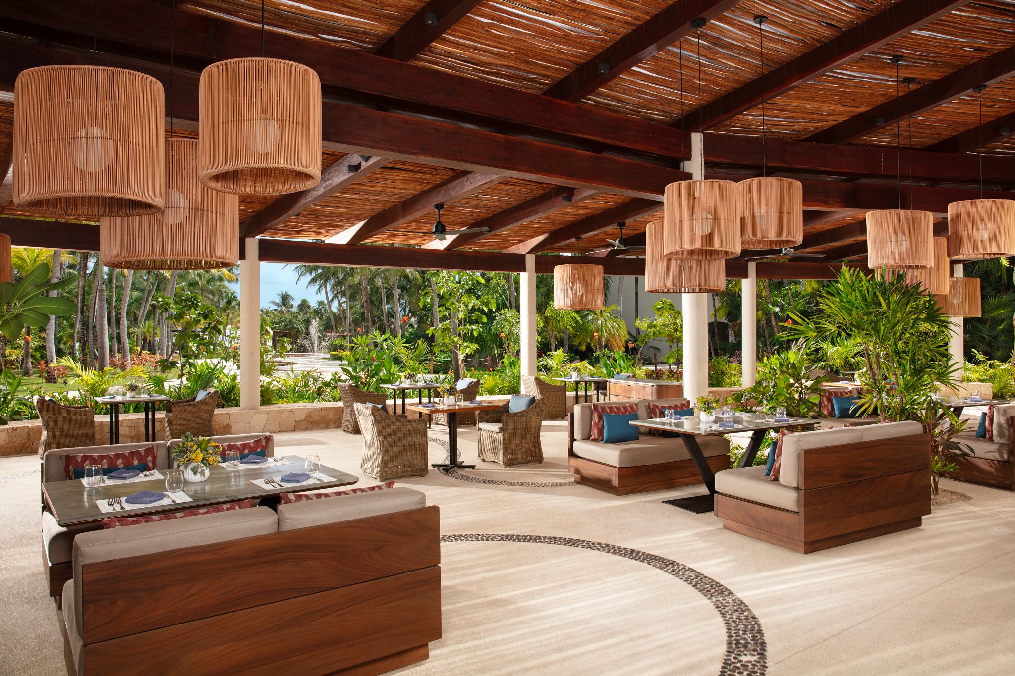 Un área lounge al aire libre con mobiliario de mimbre, lámparas colgantes y vistas a la vegetación tropical.