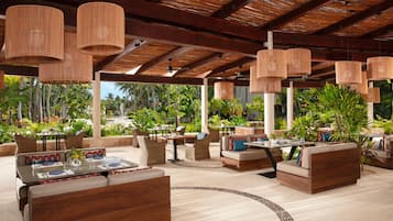 Un área lounge al aire libre con mobiliario de mimbre, lámparas colgantes y vistas a la vegetación tropical.