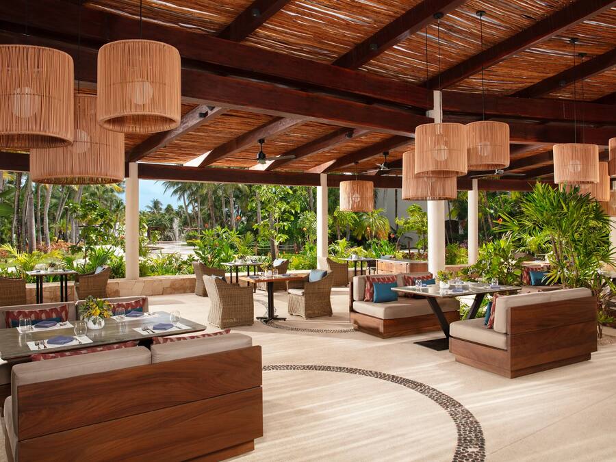 Un área lounge al aire libre con mobiliario de mimbre, lámparas colgantes y vistas a la vegetación tropical.