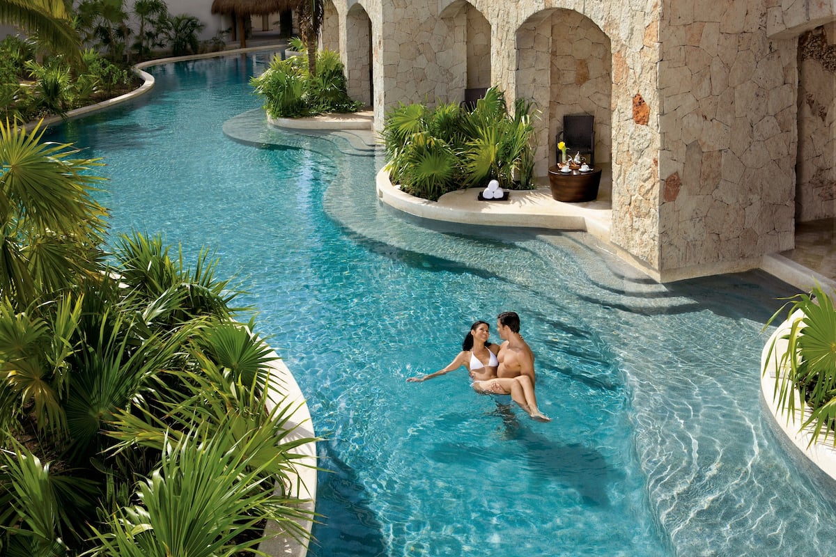 A pool area with a curved design, stone walls, and tropical plants.