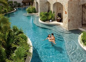 Un área de piscina con diseño curvo, paredes de piedra y plantas tropicales.