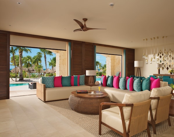 A spacious living room with a large sofa, a coffee table, and a view of a pool and palm trees.