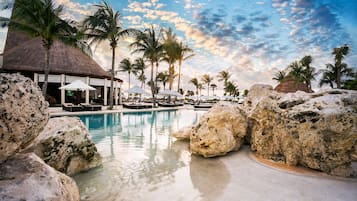 A resort pool area with lounge chairs, umbrellas, and palm trees.