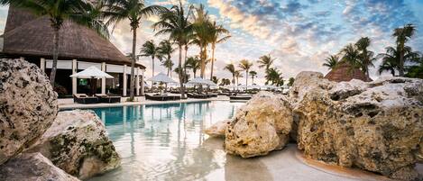 A resort pool area with lounge chairs, umbrellas, and palm trees.