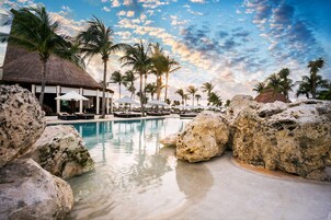 A resort pool area with lounge chairs, umbrellas, and palm trees.
