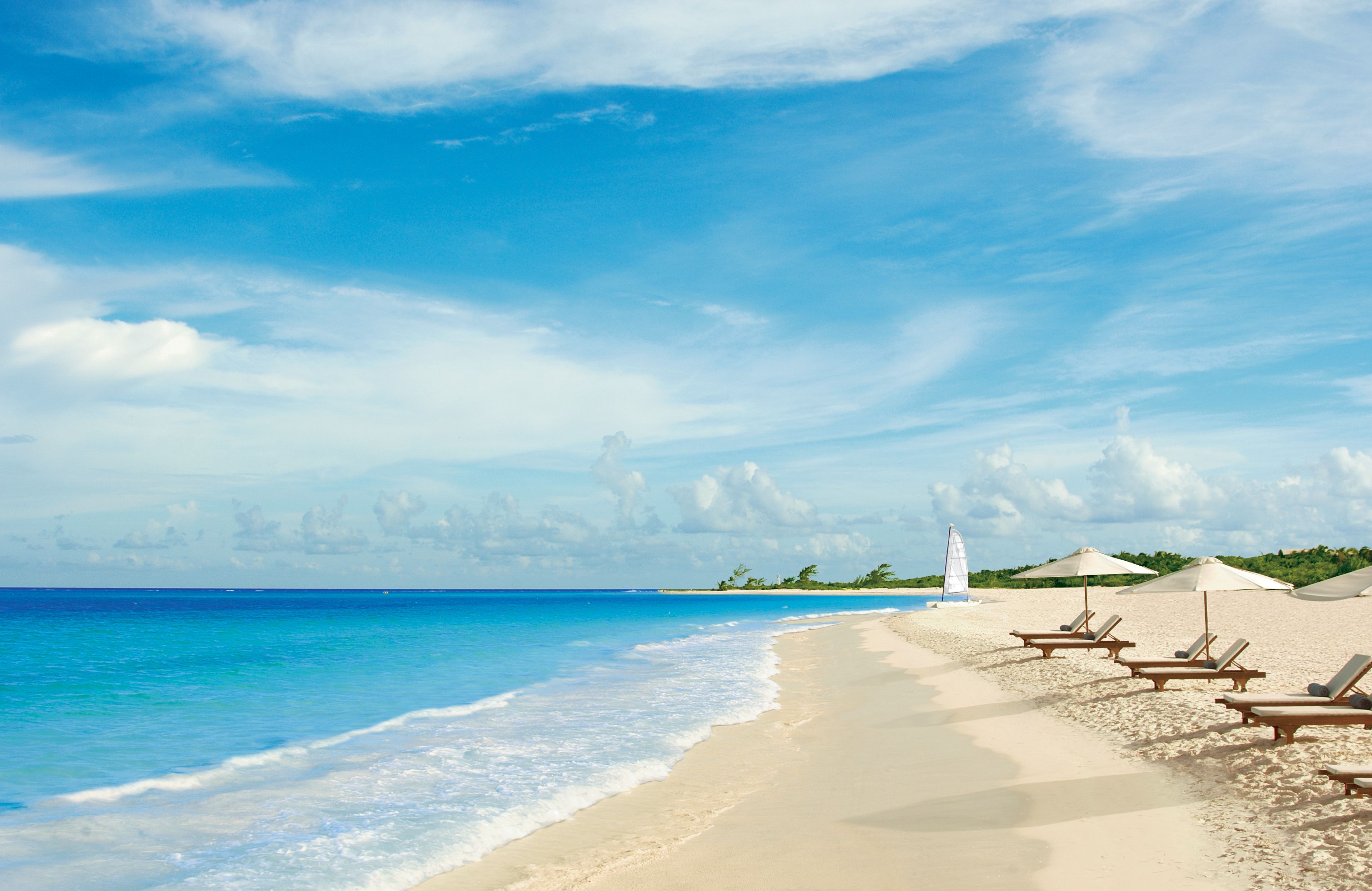 A beach with clear blue water, white sand, and a few lounge chairs.