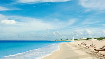 A beach with clear blue water, white sand, and a few lounge chairs.