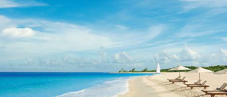 A beach with clear blue water, white sand, and a few lounge chairs.
