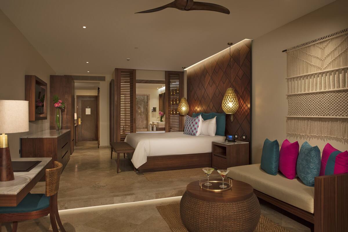 A modern hotel room with a large bed, a sofa, a dining area, and a decorative wall.